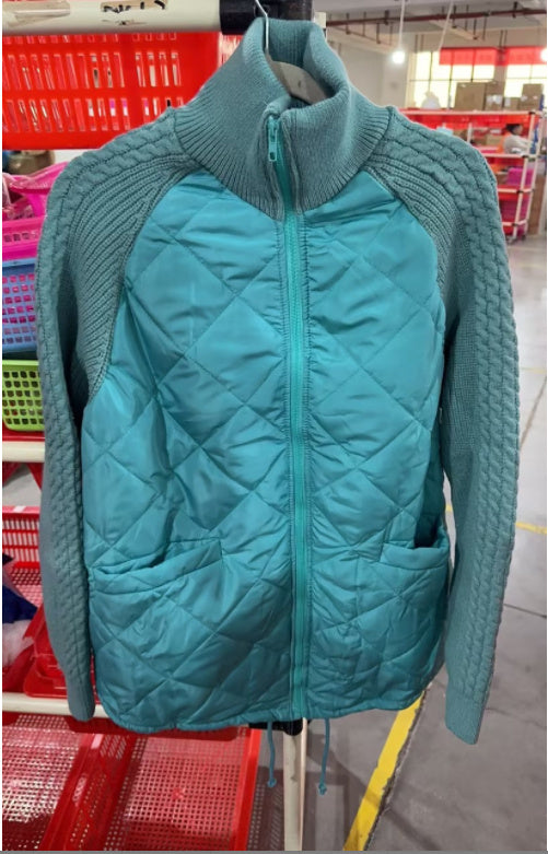 Teal quilted jacket with knitted sleeves on a hanger in a store setting