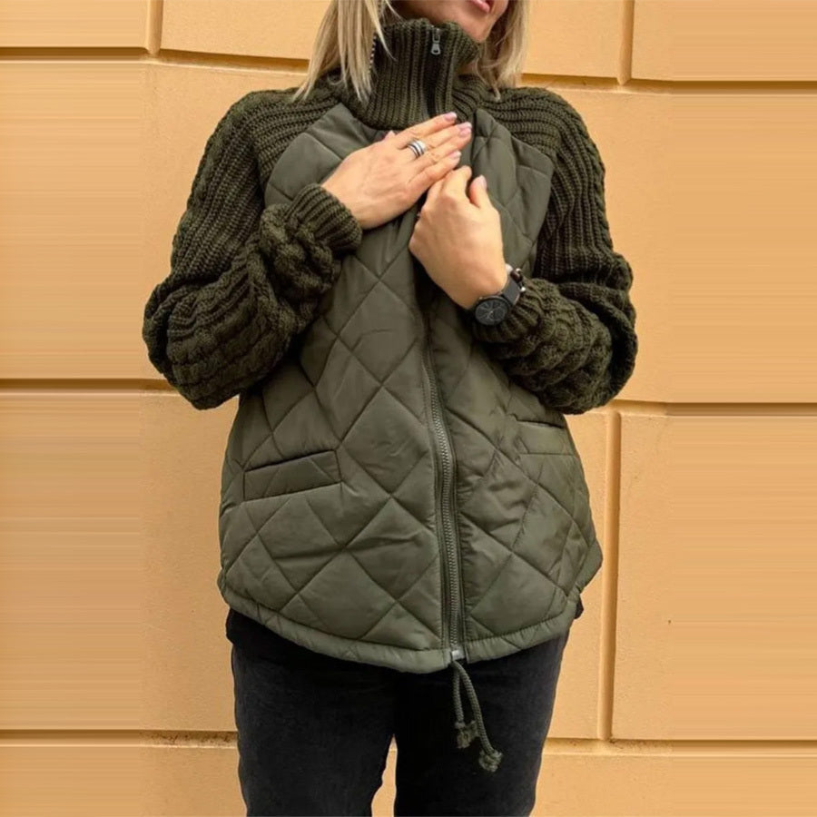 Person wearing a green quilted vest over a dark sweater against a beige wall.