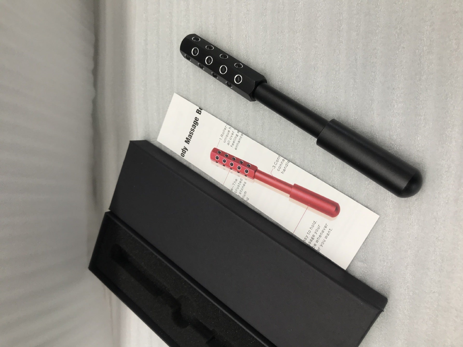 Black massage roller with red handle on a gray surface