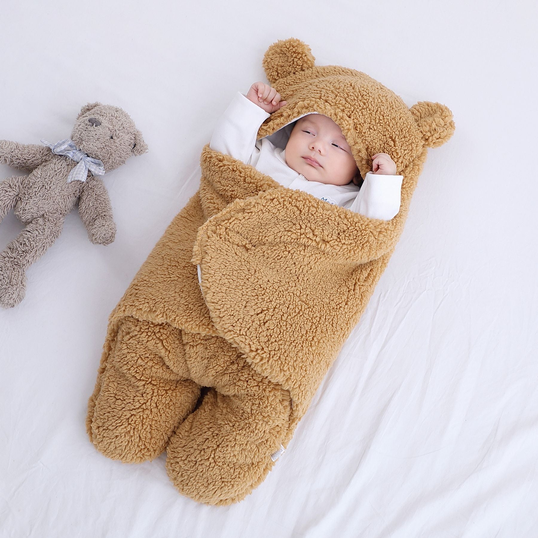 Baby in a brown bear-themed sleeping bag with a teddy bear on a white background