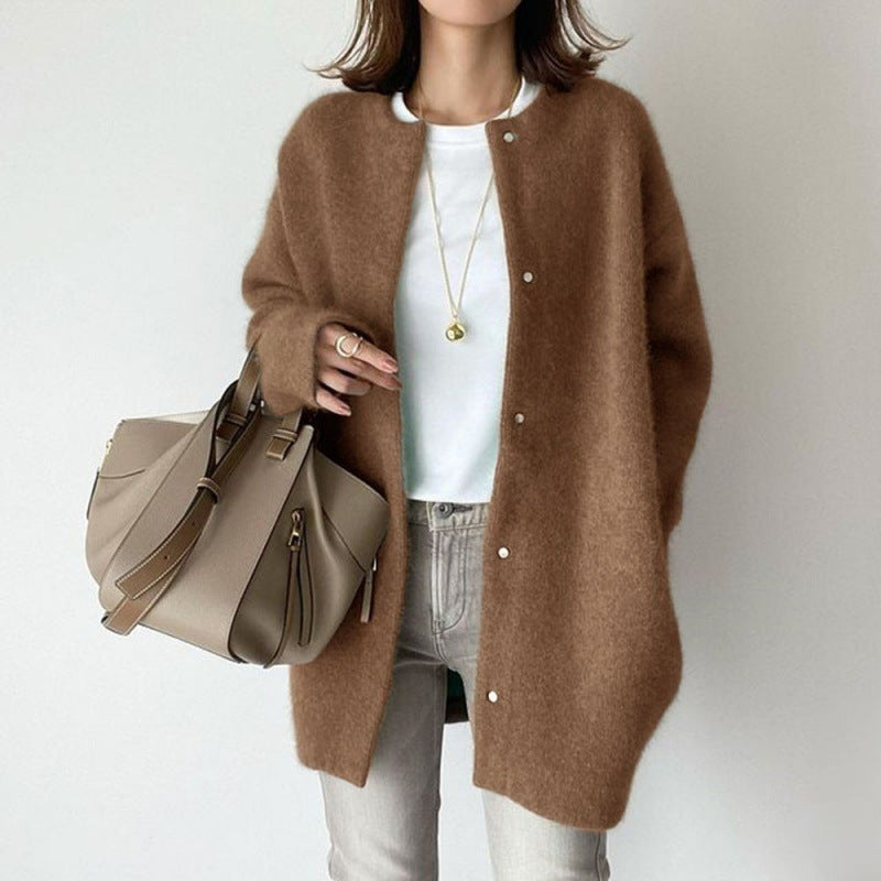 Person wearing a brown cardigan holding a beige handbag against a plain background