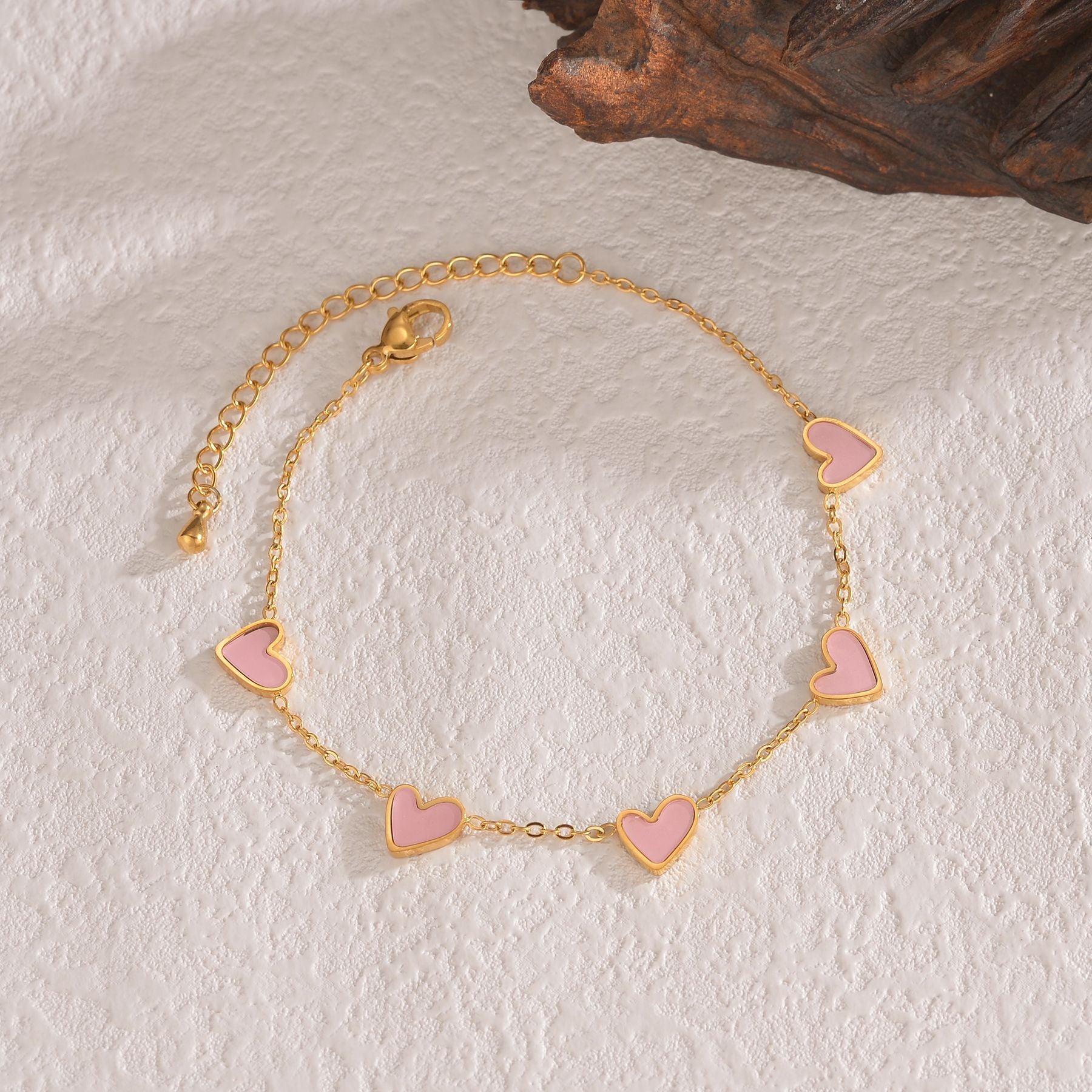 Gold bracelet with pink heart charms on a textured white surface