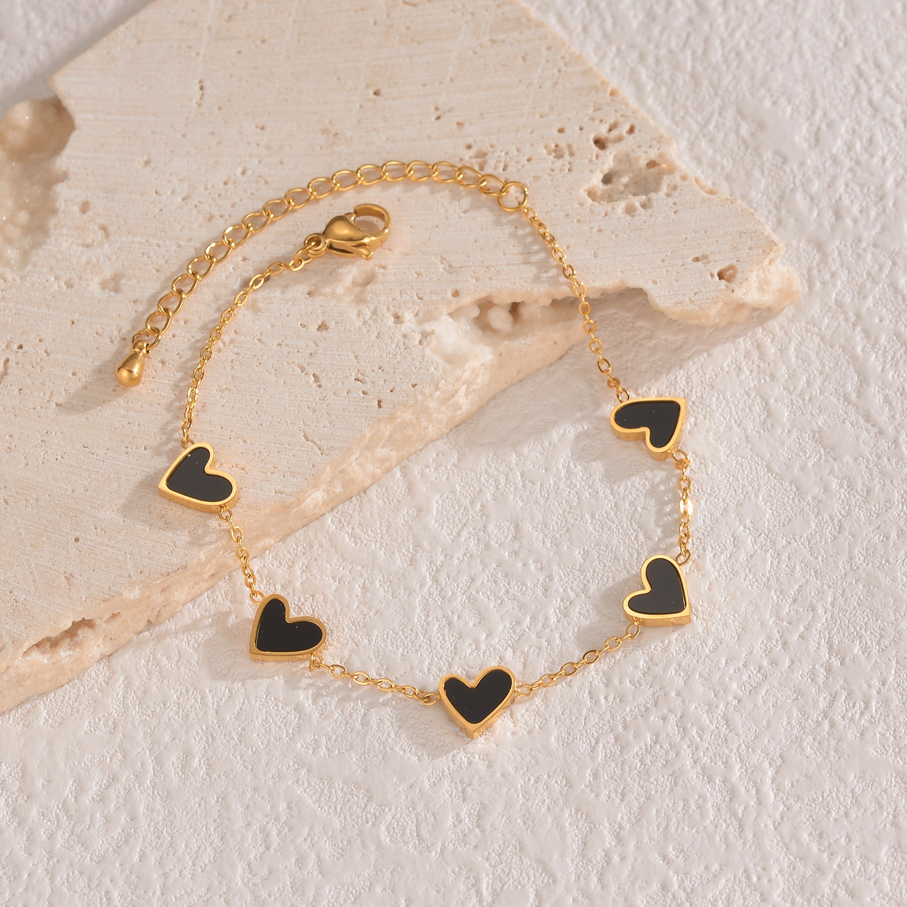 Gold bracelet with black heart charms on a textured stone surface