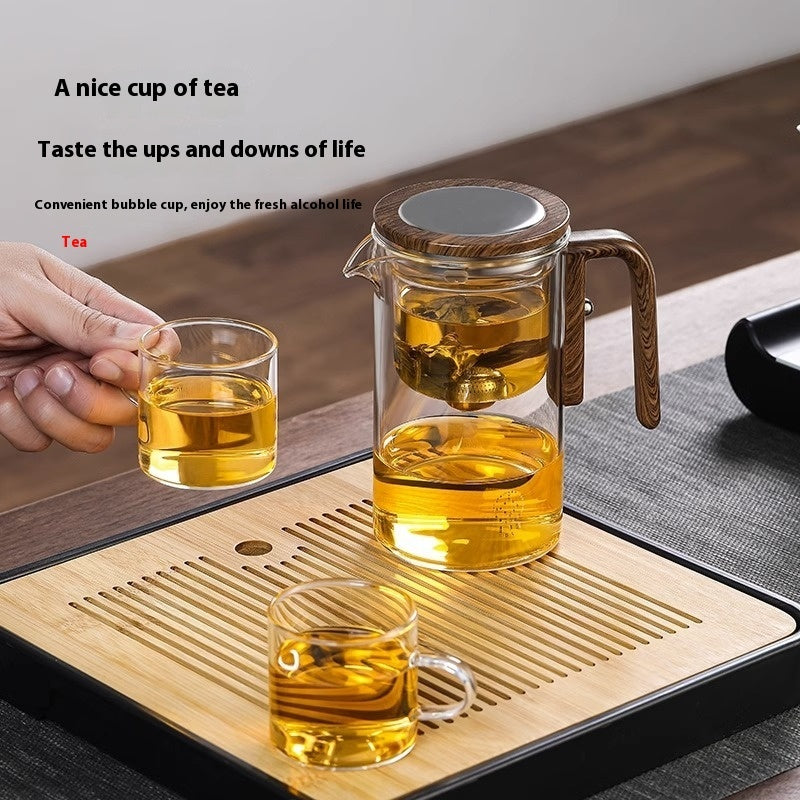 Tea-making setup with glass teapot and cups on a wooden tray.