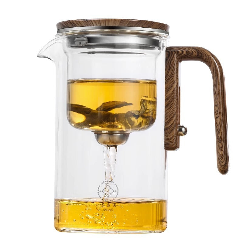 Clear glass teapot with wooden handle and lid filled with yellow liquid on a white background
