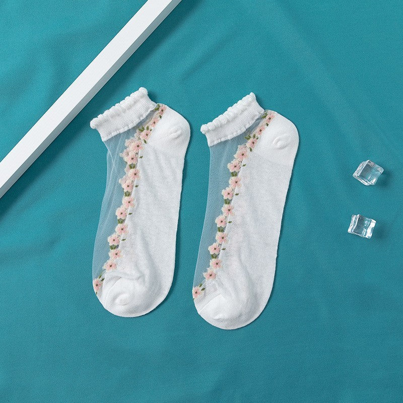 A pair of women's boat socks with a floral design in purple and white colors, worn with a pair of flat shoes.