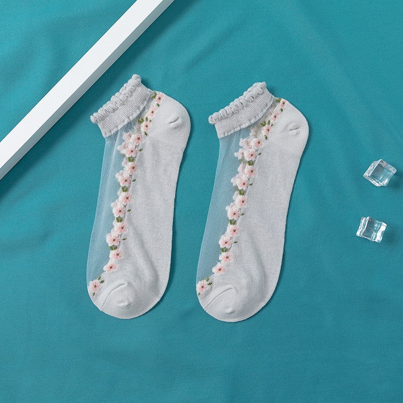 A pair of women's boat socks with a floral design in purple and white colors, worn with a pair of flat shoes.