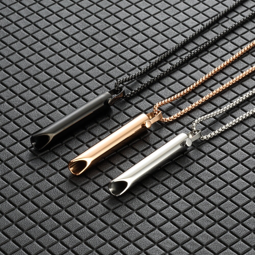 Three necklaces with cylindrical pendants in black, rose gold, and silver on a textured black surface.