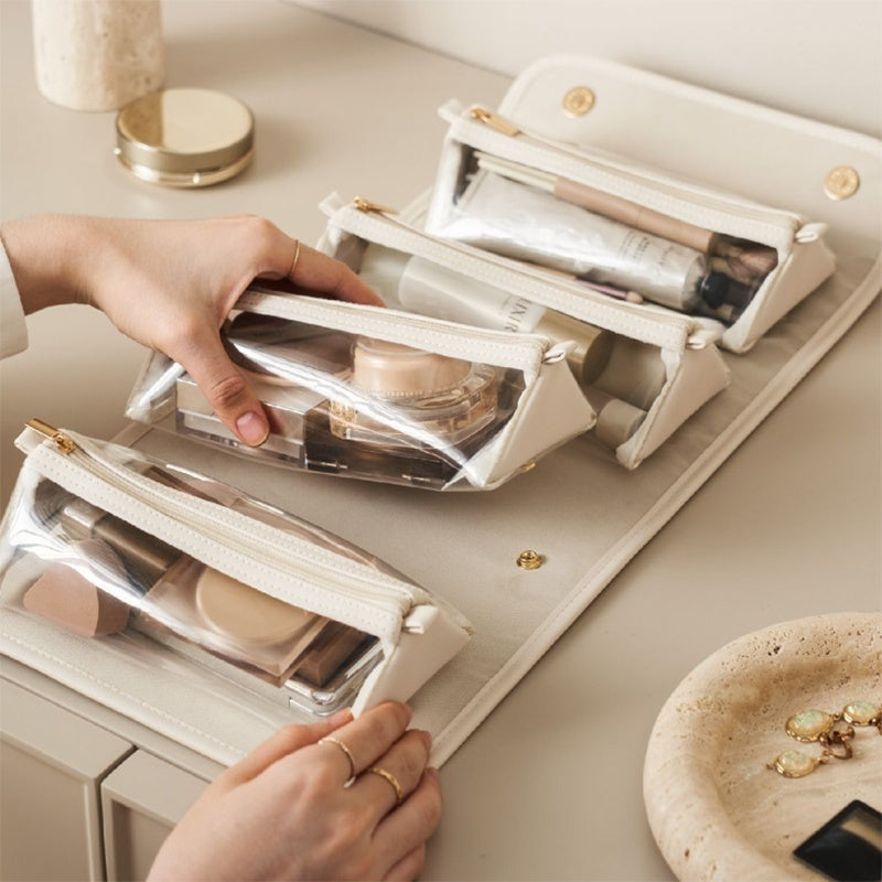 Person organizing makeup products in clear cosmetic bags on a light surface.