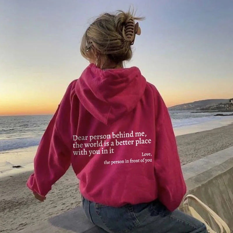 Person wearing a pink hoodie with a quote on the beach at sunset