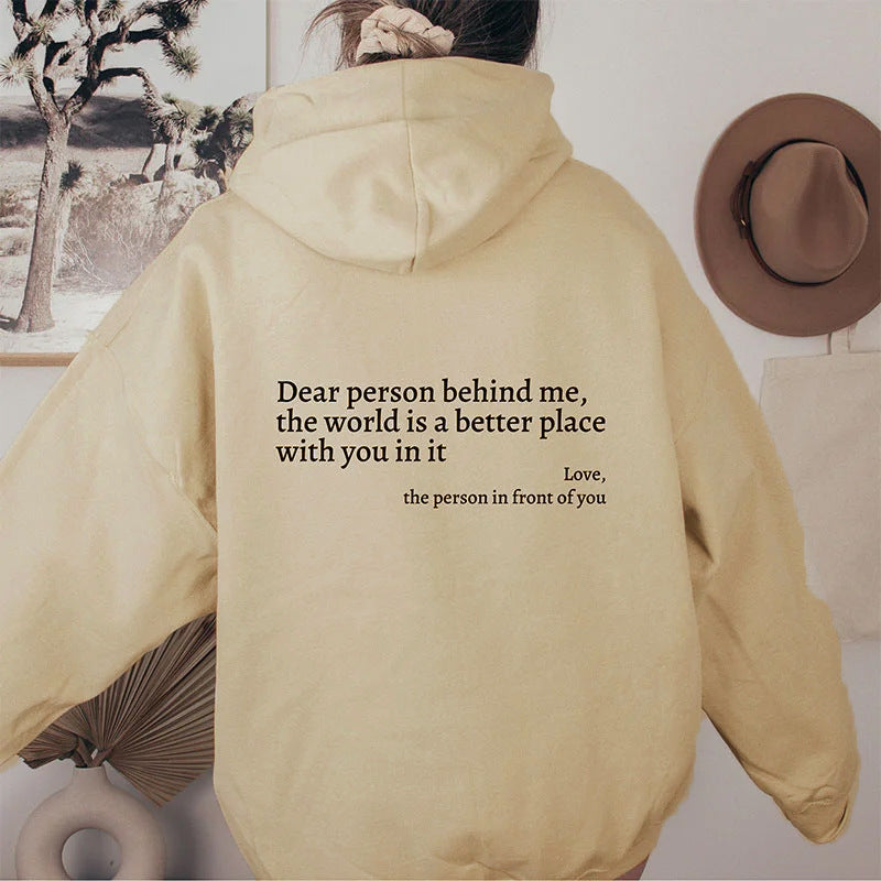 Person wearing a beige hoodie with a motivational quote on the back, standing in a room with decor elements.