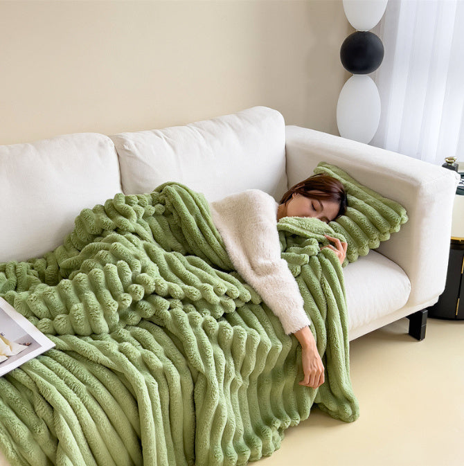 Person lying on a white couch under a green blanket in a cozy living room.