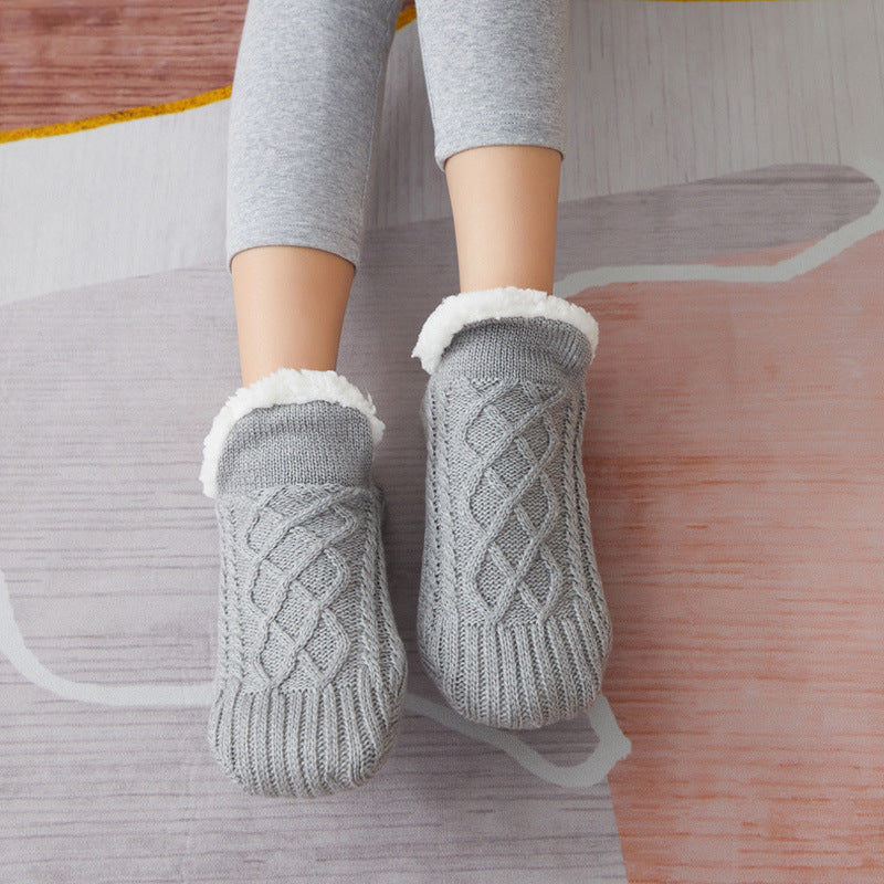 Gray knitted socks with white fur trim worn by a person on a wooden floor.