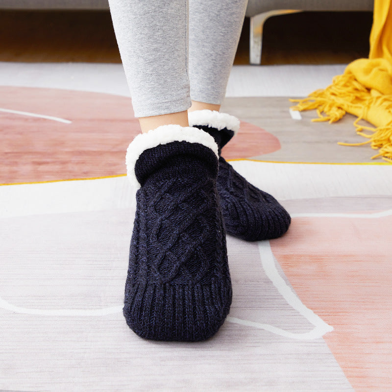 Person wearing dark blue cable knit socks with white fur trim on a wooden floor.