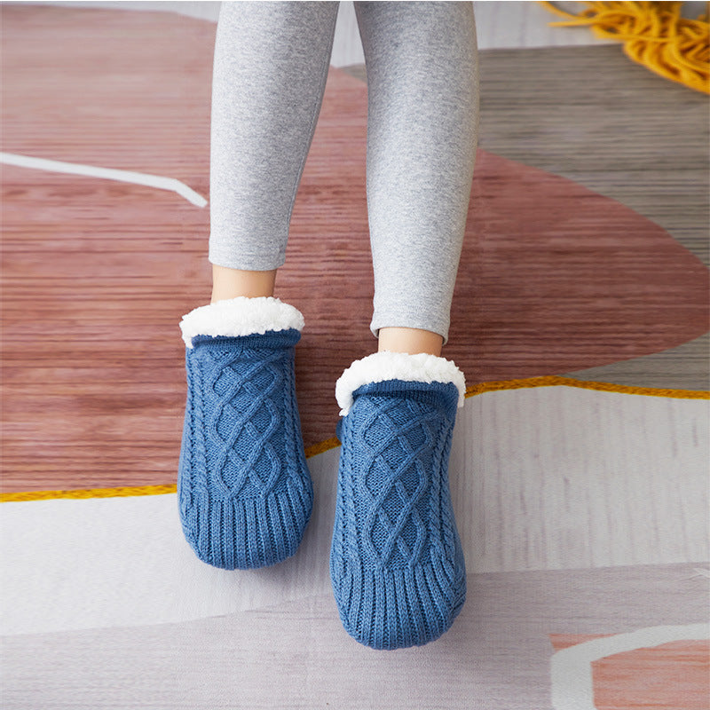 Blue knitted slippers with white fur trim worn by a person on a wooden floor.