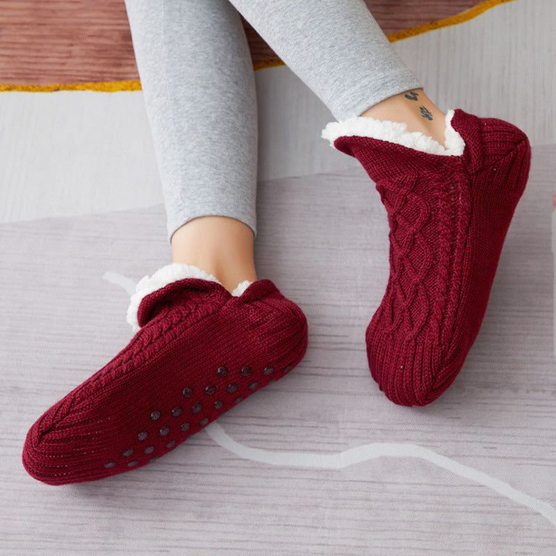 Red knitted slippers with white fur lining worn by a person on a light wooden floor.