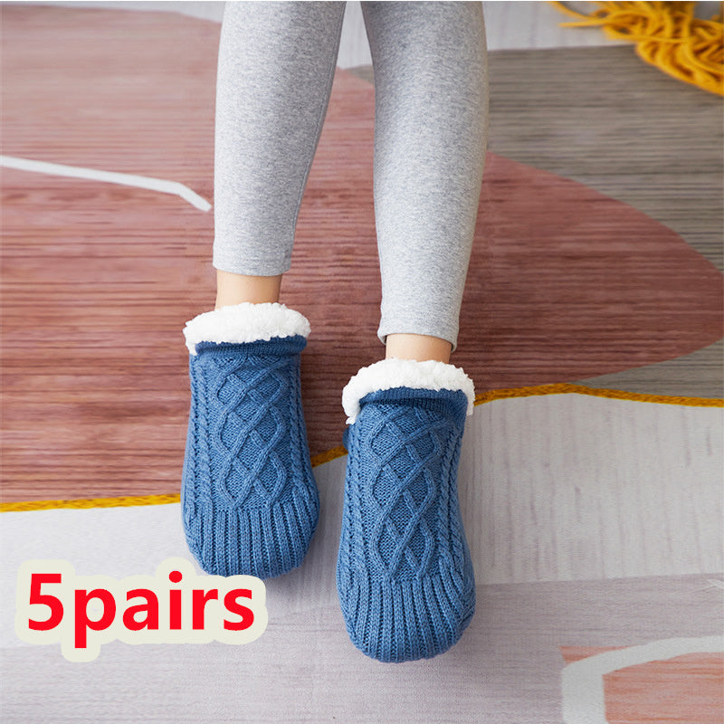 Blue knitted slippers with white fur lining worn by a person on a wooden floor.