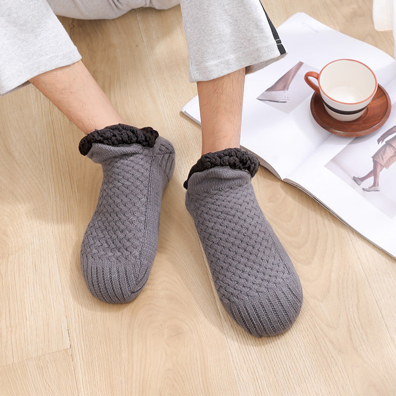 Person wearing gray textured slippers on a wooden floor with a magazine and cup in the background.
