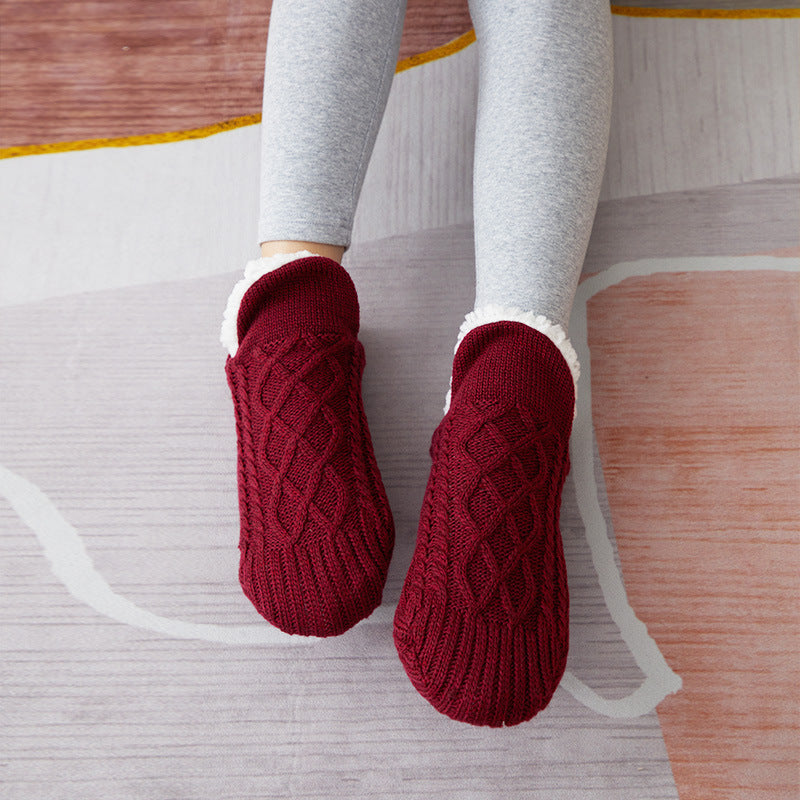 Red knitted slippers worn with gray leggings on a wooden floor.