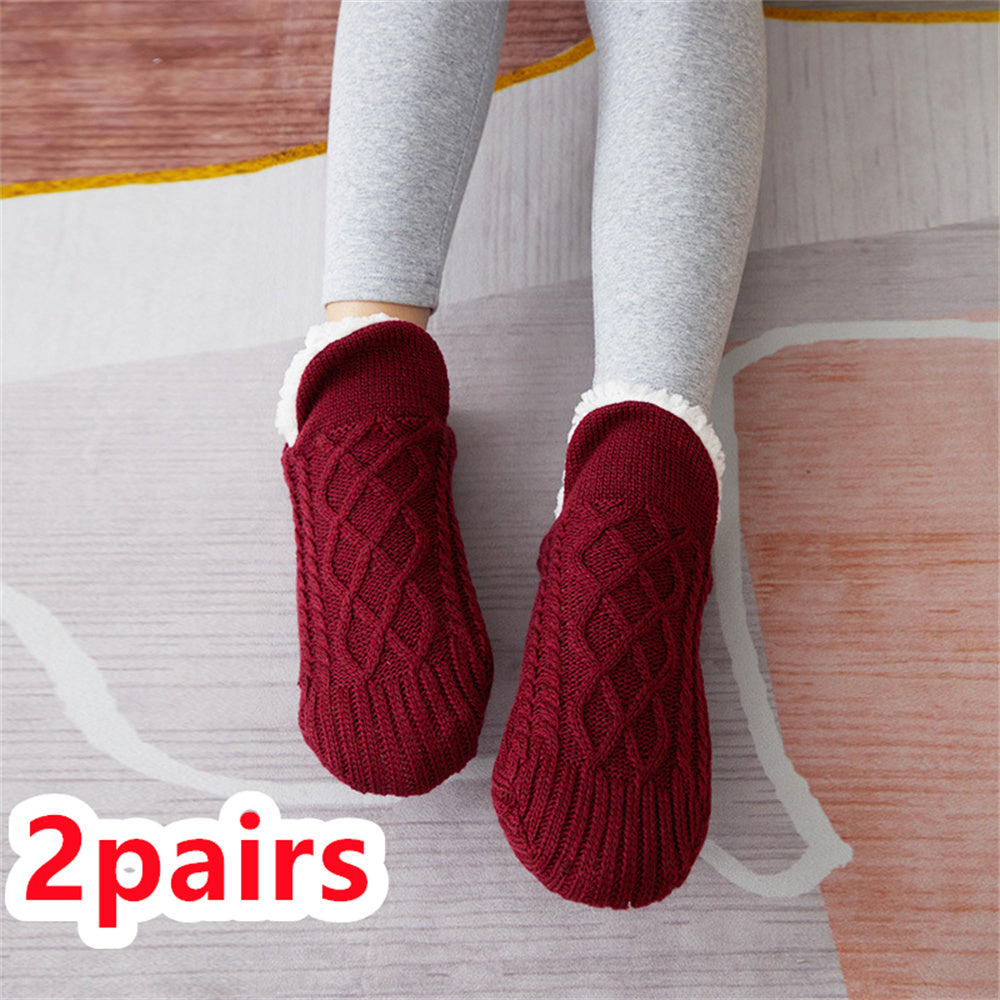 Red knitted socks with white soles worn by a person on a wooden floor.