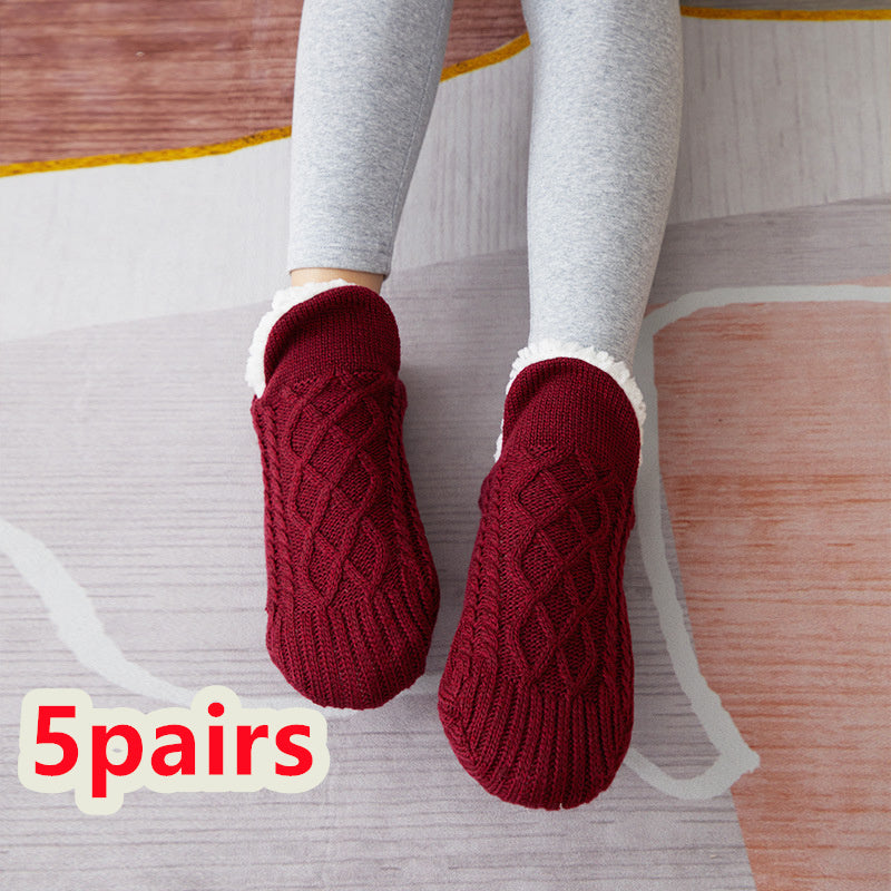 Red knitted slippers worn with gray leggings on a wooden floor.