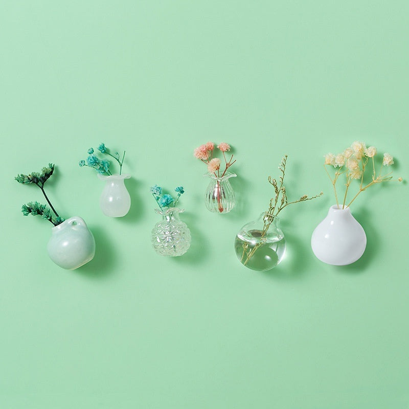 Set of small decorative vases with plants on a light green background